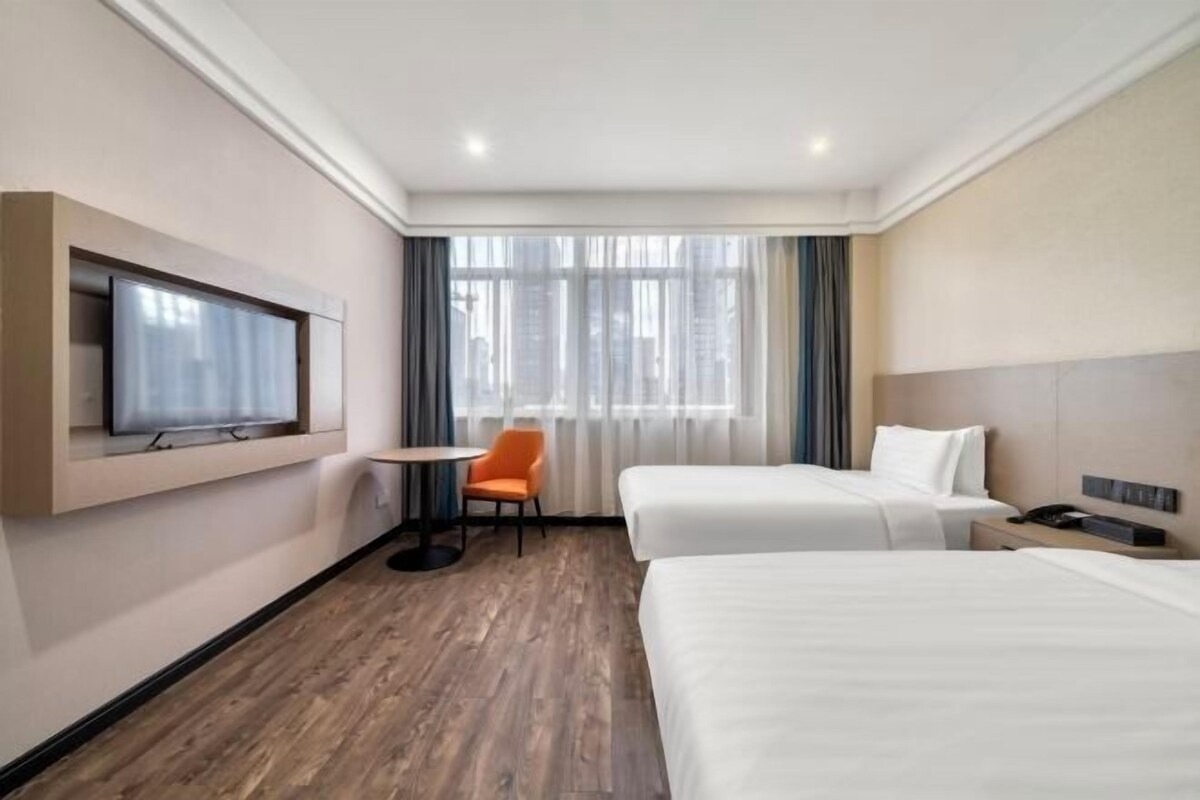 A hotel room with two beds, a TV, a small table, and a chair.