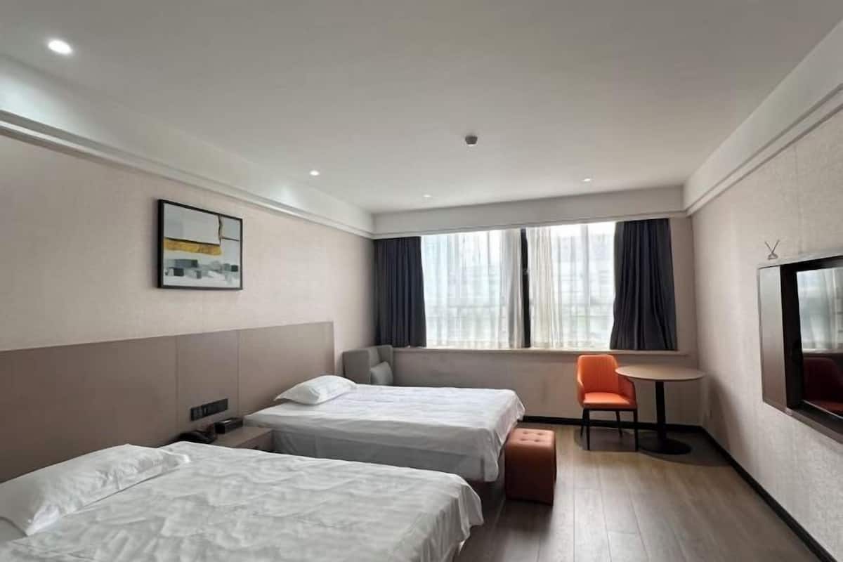 Ein Hotelzimmer mit zwei Betten, einem kleinen Tisch, einem Sessel und einem Fernseher.
