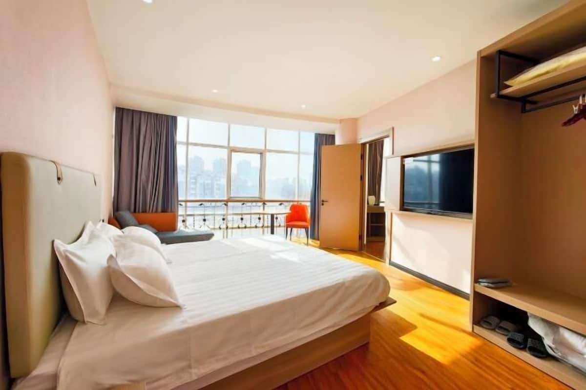 Ein Hotelzimmer mit Bett, Fernseher, Kleiderschrank und einem Balkon mit Blick auf die Stadt.