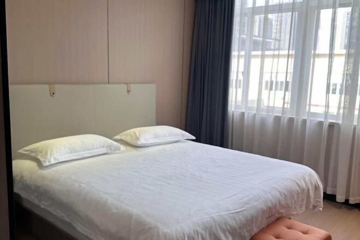 A bed with white bedding, a headboard, and a window with curtains.