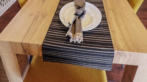 Un'area pranzo con un lungo tavolo di legno apparecchiato per sei persone, sedie gialle e un runner da tavolo decorato.