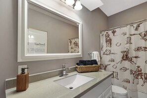 A bathroom with a large mirror, a sink, a shower curtain with animal prints, and a basket of towels. - Spacious 5BD - UNL 5mins - BBQ, Games & Backyard (Lincoln)