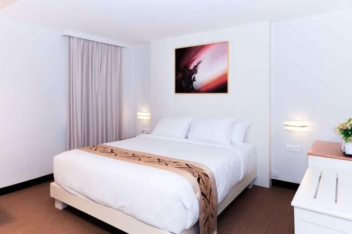 A hotel room with a bed, a nightstand, a wall-mounted lamp, and a painting.