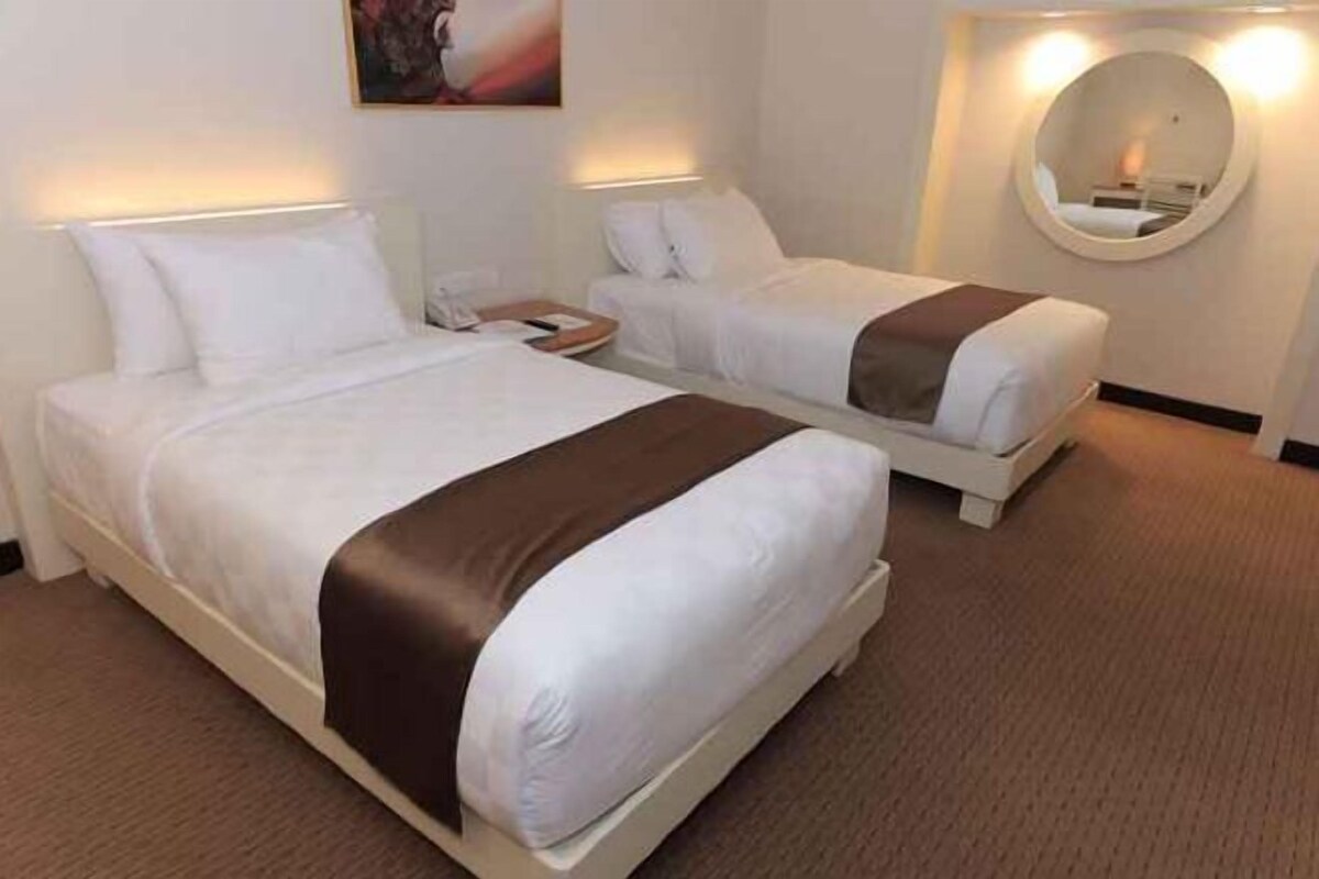 Ein Hotelzimmer mit zwei Betten, einem runden Spiegel und einer Wandleuchte.