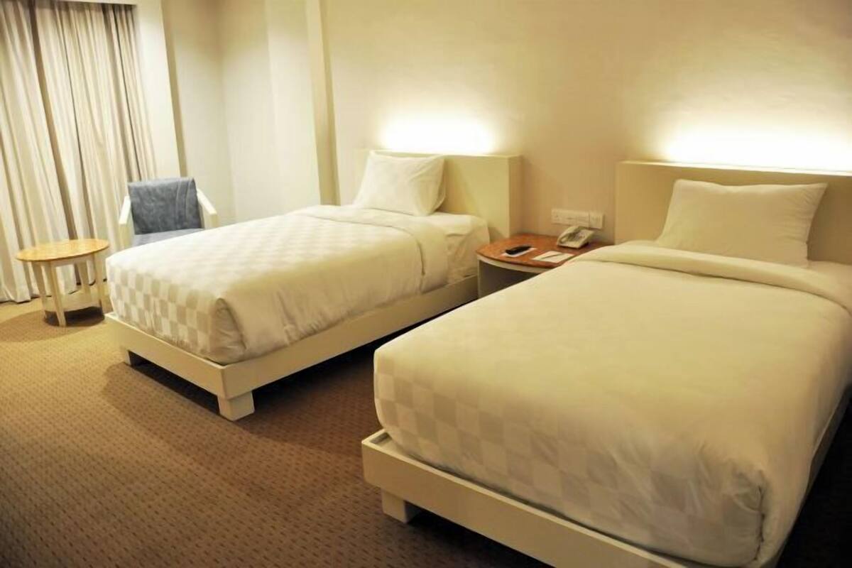 Une chambre d’hôtel avec deux lits, une chaise, une petite table et une lampe.