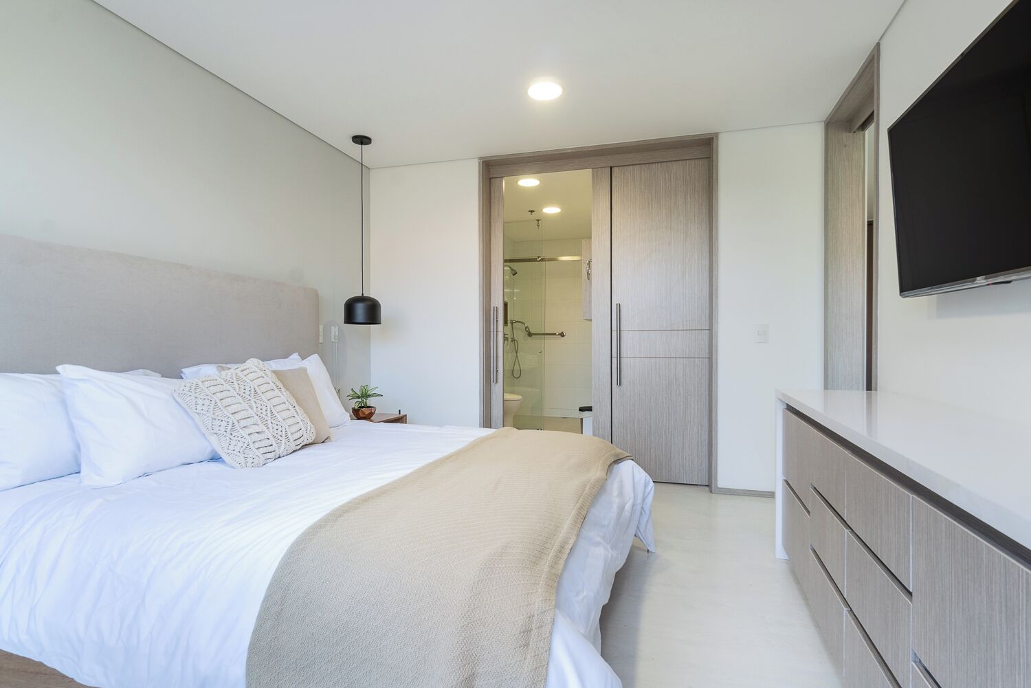 Un dormitorio moderno con cama, mesita de noche y televisor en la pared.