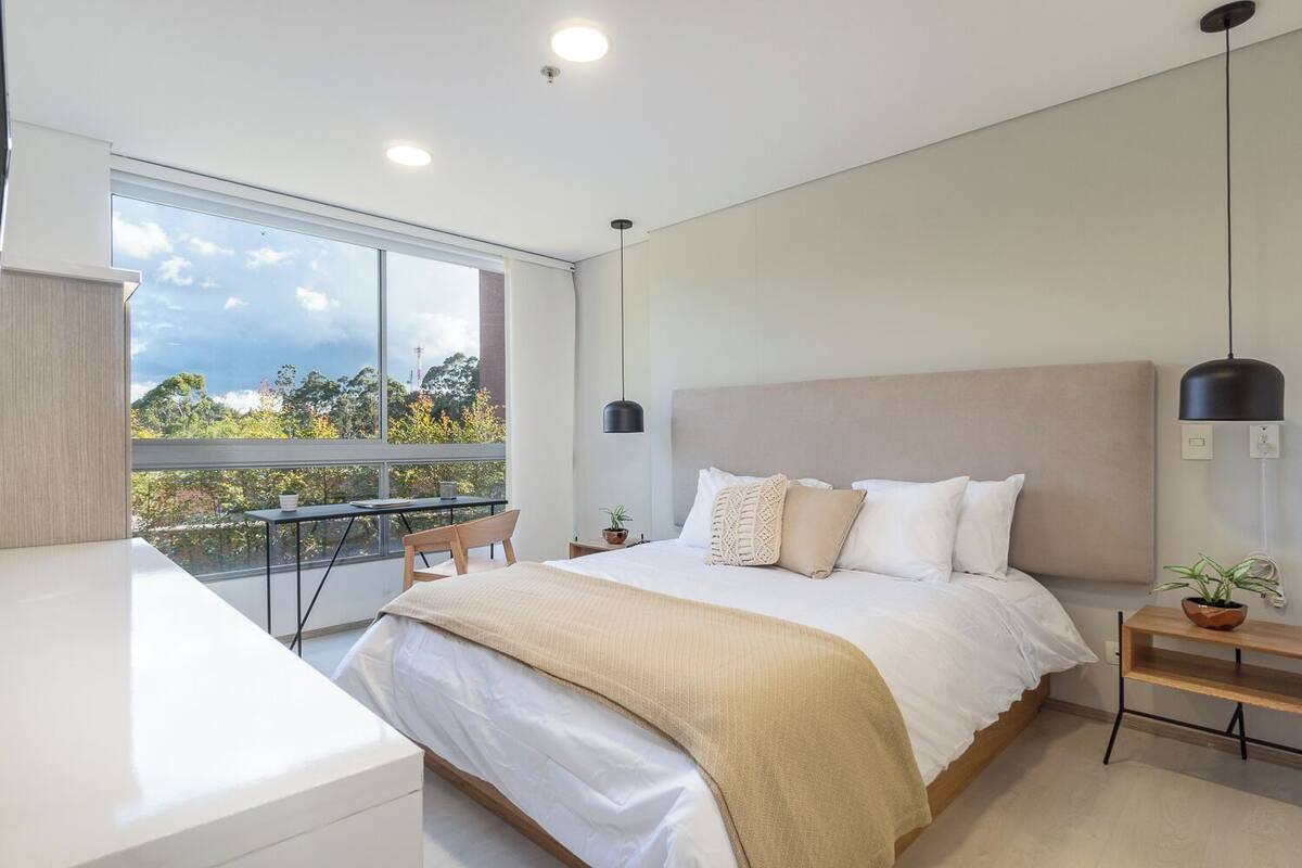 A modern bedroom with a large bed, a desk, and a balcony with a view.