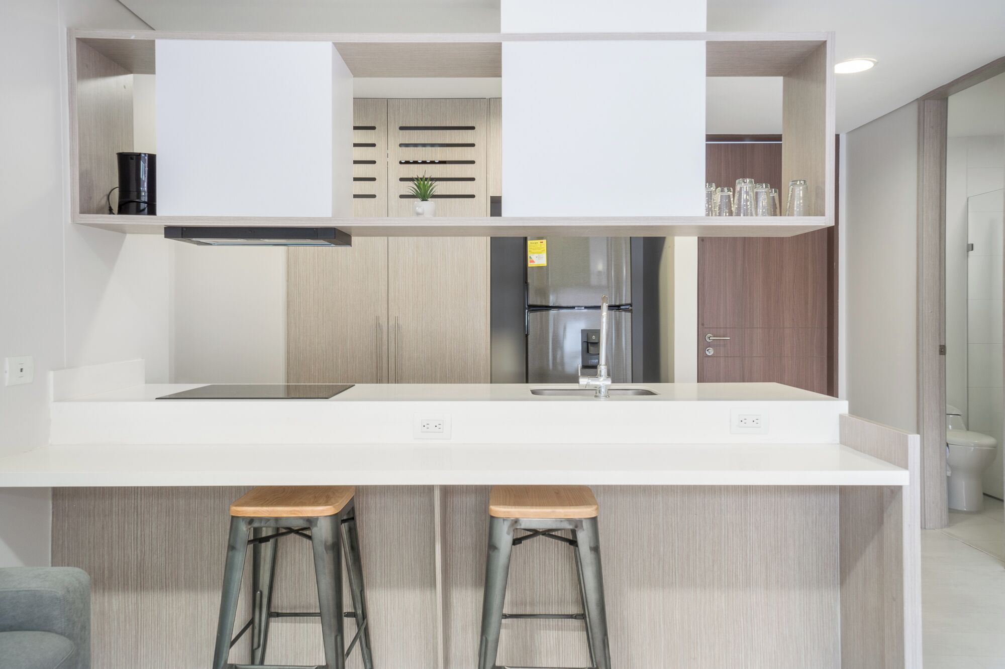 A modern kitchen with a white countertop, stainless steel appliances, and wooden bar stools.