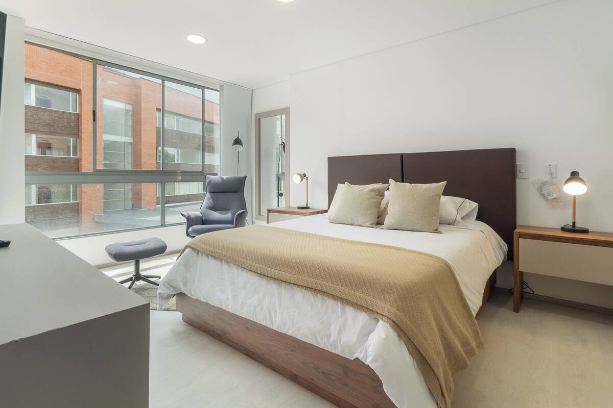 A modern bedroom with a large bed, a desk, and a chair.