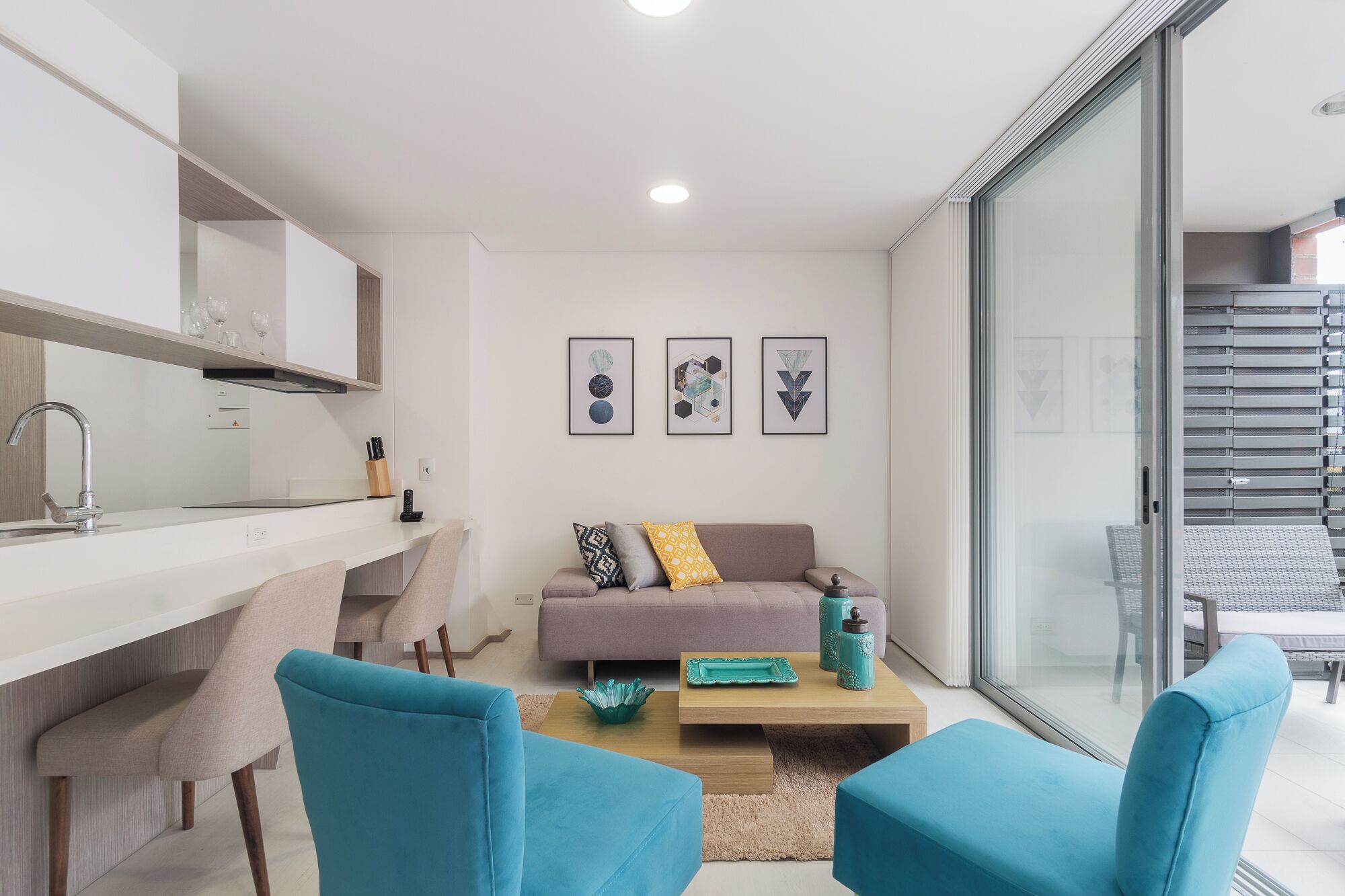 A modern living room with a sofa, two blue chairs, a coffee table, and a kitchen area with a sink and countertop.