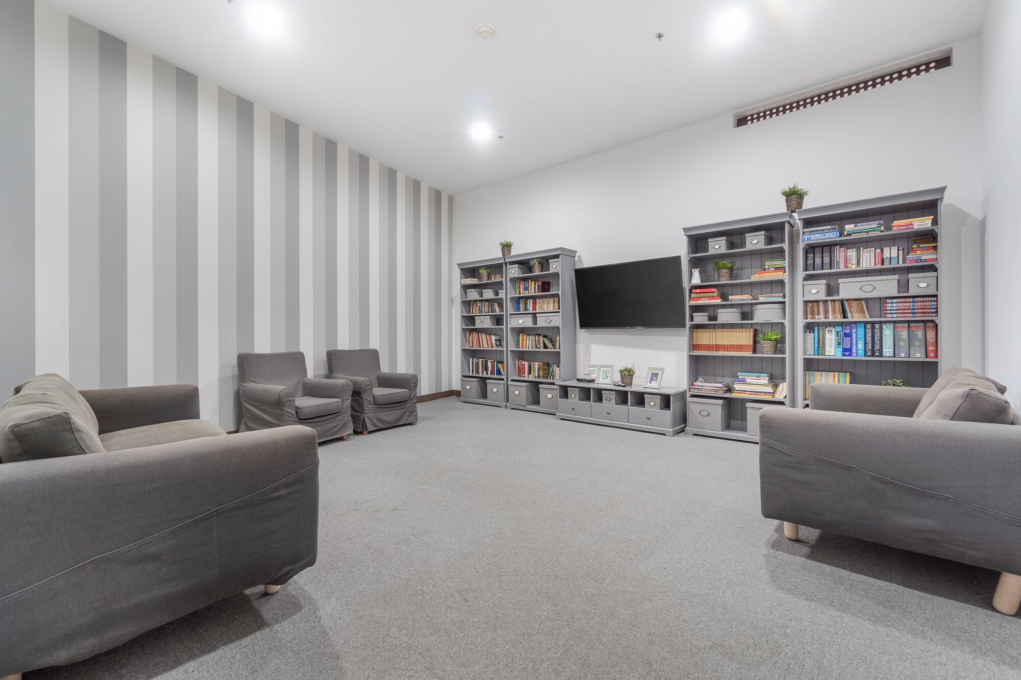 Un soggiorno moderno con divani grigi, una TV a schermo piatto e due ampie librerie piene di libri e oggetti decorativi.