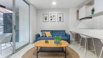 A modern living space with a blue sofa, a wooden coffee table, and a kitchen area with white cabinets and bar stools.