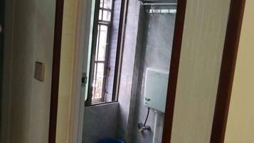 A narrow hallway with a window, a blue trash bin, and a white wall-mounted device.