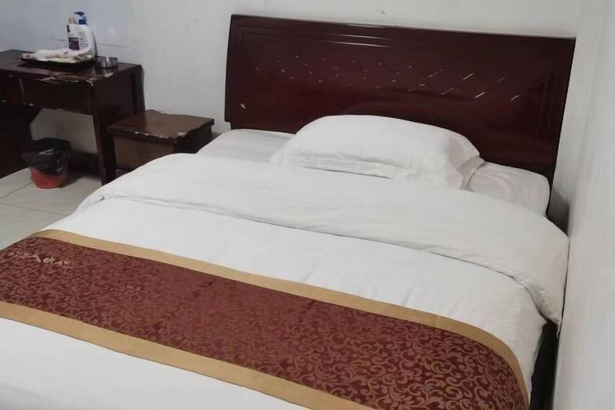Een bed met hoofdbord, een nachtkastje met een fles en een kleine prullenbak.