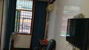 A room with a TV, a fan, a table, and a window with curtains. - Enshi Xueyuan Hotel (Enshi City)