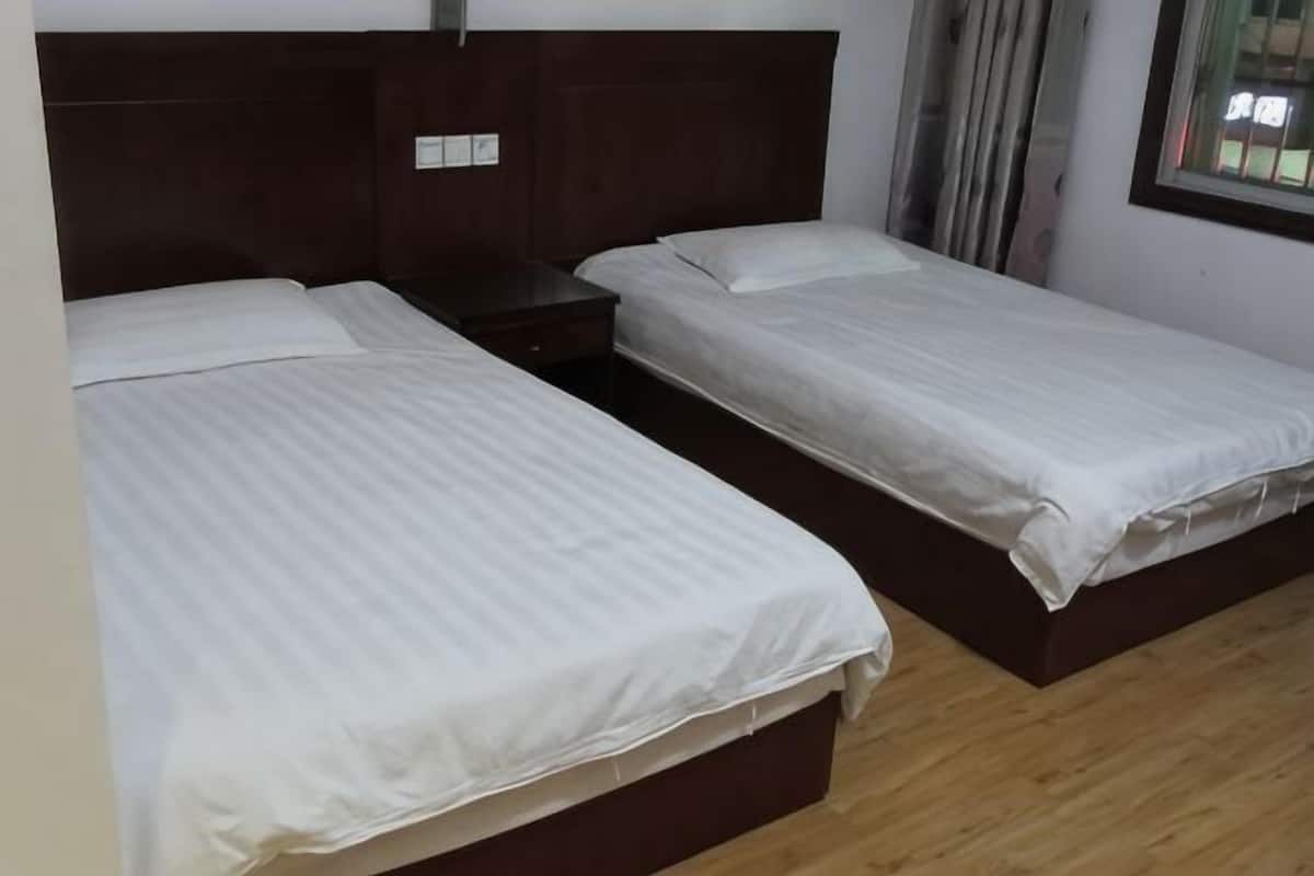 Een kamer met twee enkele bedden, houten hoofdborden, een klein nachtkastje en een raam met gordijnen.