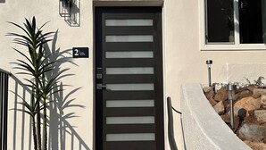 Un edificio moderno con una puerta negra, felpudo y una planta en maceta.
