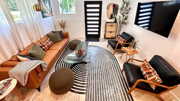 Una sala de estar moderna con un sofá de cuero marrón, alfombra a rayas blanco y negro y una mesa de centro redonda.