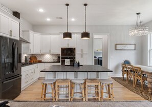 A modern kitchen with white cabinetry, a central island with stools, a dining area with a table and chairs, and pendant lighting. - Lakeside Bliss w/Dock, Kayaks, Fire Pit, Foosball (Estill Springs)