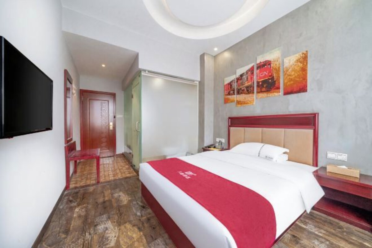 A hotel room with a large bed, a TV mounted on the wall, and a red carpet leading to a door.