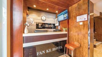 Un mostrador de recepción con un reloj, una pantalla digital y un cartel con el nombre del hotel.