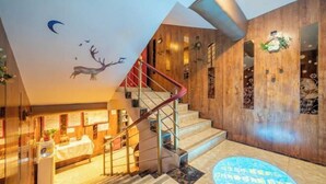 Un moderno vestíbulo de hotel con interior de madera, una escalera con barandilla roja y un mural de un ciervo en el techo.