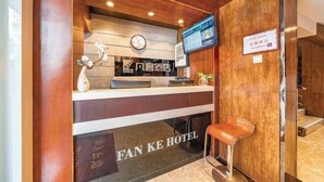 Mostrador de recepción con un reloj, un televisor y un cartel anunciando el Hotel Fan Ke.