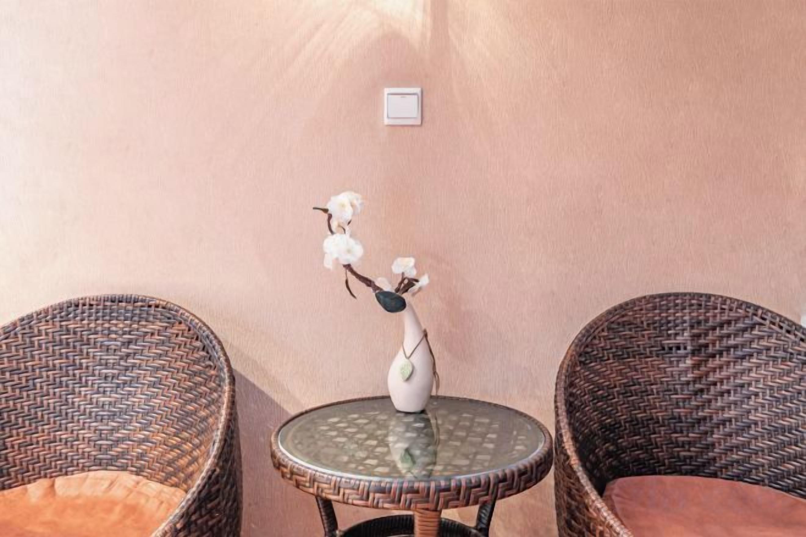 A wicker chair, a round table with a vase, and a wall-mounted light fixture.