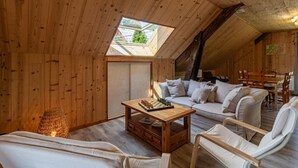 Une pièce mansardée chaleureuse avec des murs en bois, un plafond en pente, un puits de lumière, un canapé, une table basse et un coin repas.