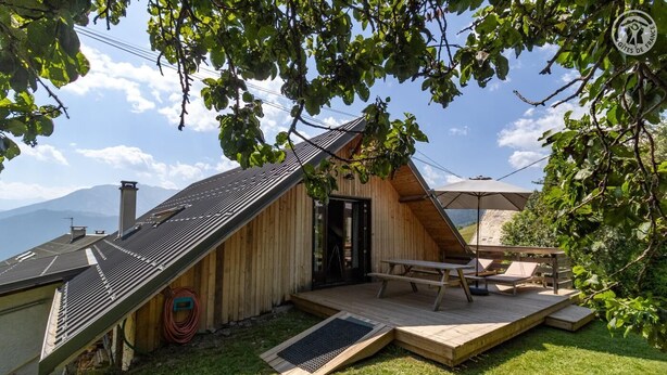 Une cabane en bois avec un toit en pente, une terrasse avec une table et des chaises, et une vue sur les montagnes.
