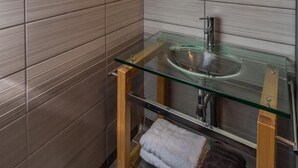 Une salle de bain moderne dotée d’un puits de lumière, d’un lavabo en verre et de lambris en bois.