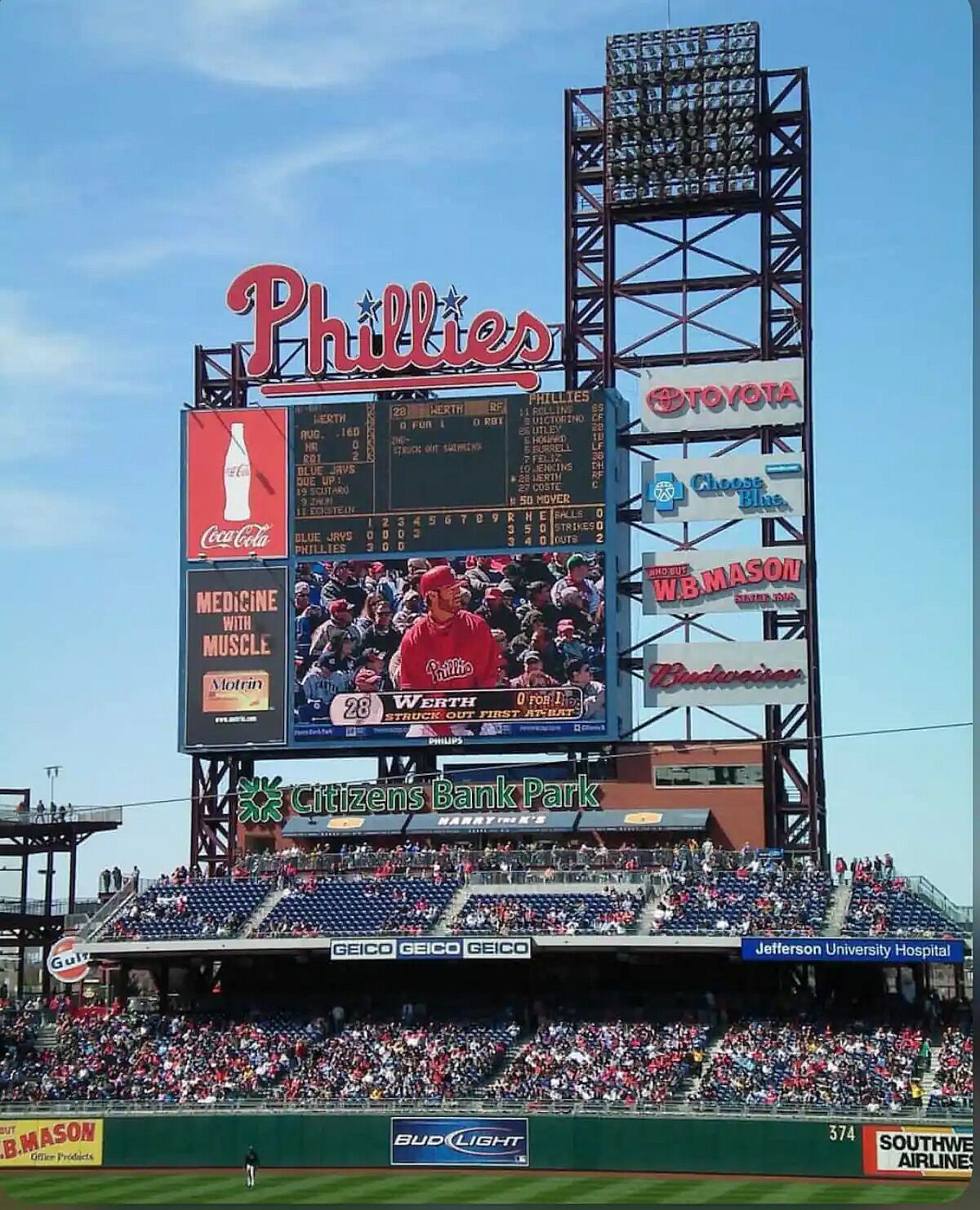 A baseball stadium with a large digital scoreboard displaying team names and scores.