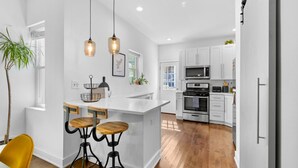 A modern kitchen with white cabinetry, a central island with stools, stainless steel appliances, and pendant lighting. - Bright & Modern: Minutes to Stadium/ Passyunk/ Airport (Philadelphia)