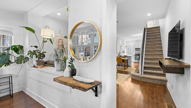 A modern interior with a white brick wall, a round mirror, a wooden bench, and a staircase leading to a dining area. - Bright & Modern: Minutes to Stadium/ Passyunk/ Airport (Philadelphia)