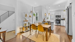 A modern kitchen with white cabinets, a dining area with a wooden table and yellow chairs, and a staircase on the left. - Bright & Modern: Minutes to Stadium/ Passyunk/ Airport (Philadelphia)