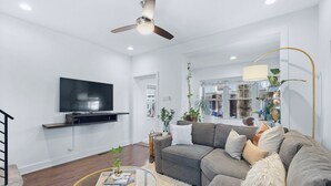 A modern living room with a grey sofa, a round coffee table, a mounted TV, and a ceiling fan. - Bright & Modern: Minutes to Stadium/ Passyunk/ Airport (Philadelphia)