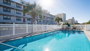 A swimming pool with a white fence, lounge chairs, and palm trees.
