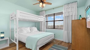 A bunk bed room with a window, curtains, a ceiling fan, and a small table with a lamp.