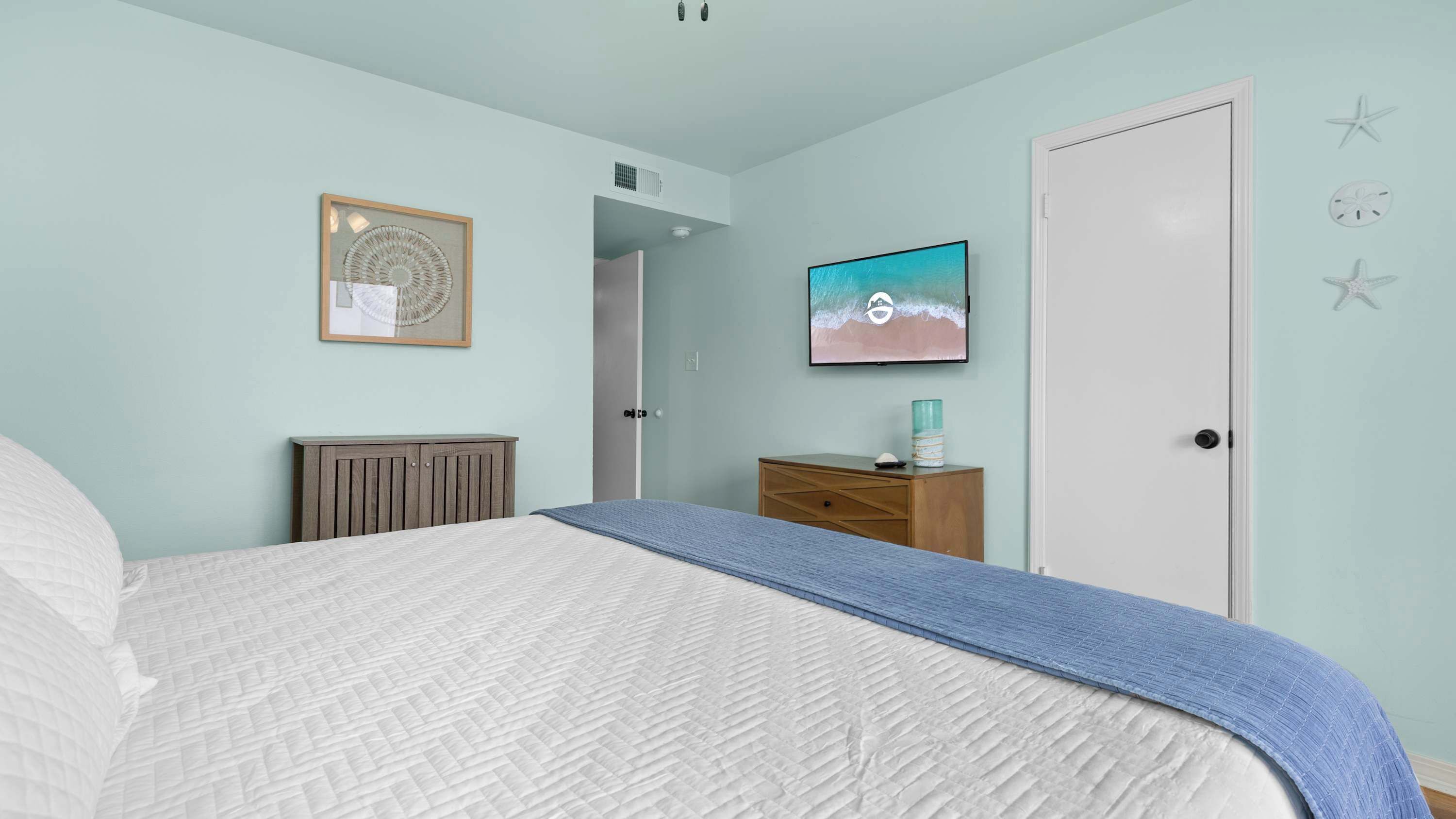 Un dormitorio con una cama, un aparador, una obra de arte enmarcada y un televisor instalado en la pared.