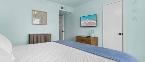 A bedroom with a bed, a dresser, a framed artwork, and a wall-mounted TV.