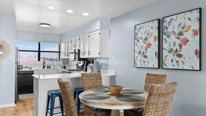 A modern kitchen with white cabinets, a central island, and a dining area with wicker chairs and a round table.