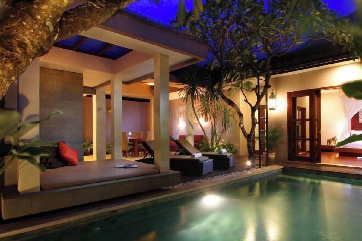 A poolside area with a seating area, a covered section, and a view of the pool.