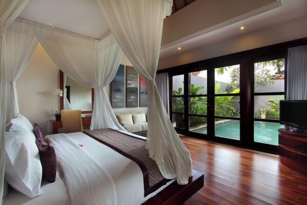 A bedroom with a canopy bed, a view of an outdoor swimming pool, and a television on a wooden stand. - Aria Exclusive Villas & Spa (Bali)