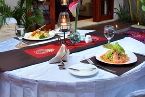 A table set with plates of food, glasses, and a candle. - Aria Exclusive Villas & Spa (Bali)
