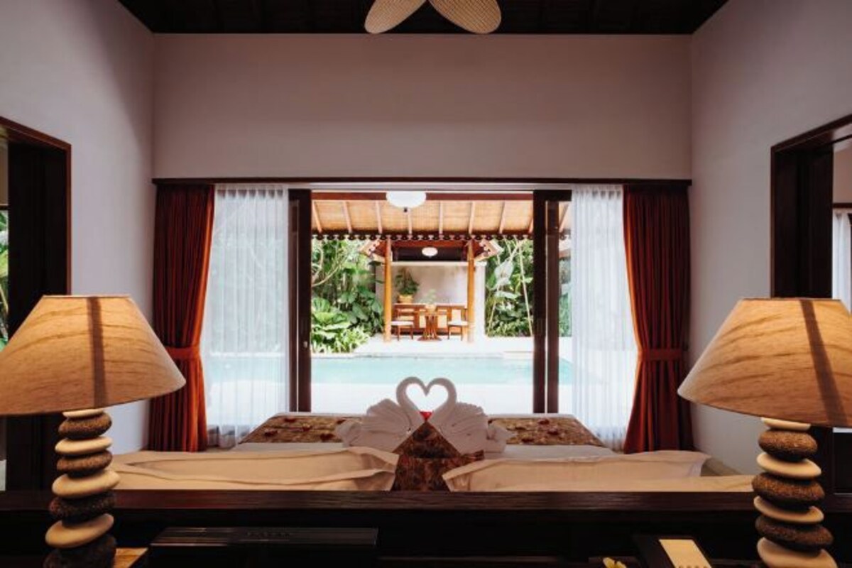 A room with a bed, two lamps, and a view of an outdoor seating area.