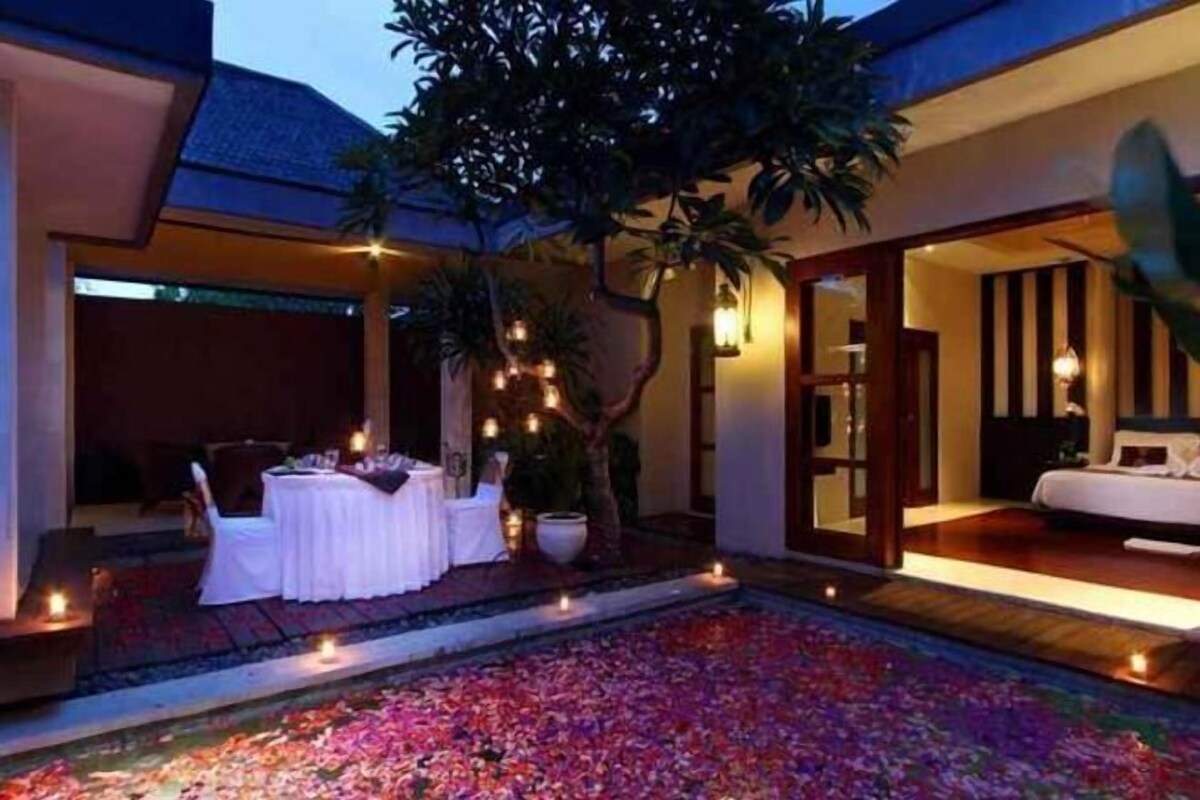 A pool area with a water feature, a dining setup with tables and chairs, and a bedroom visible through an open door.