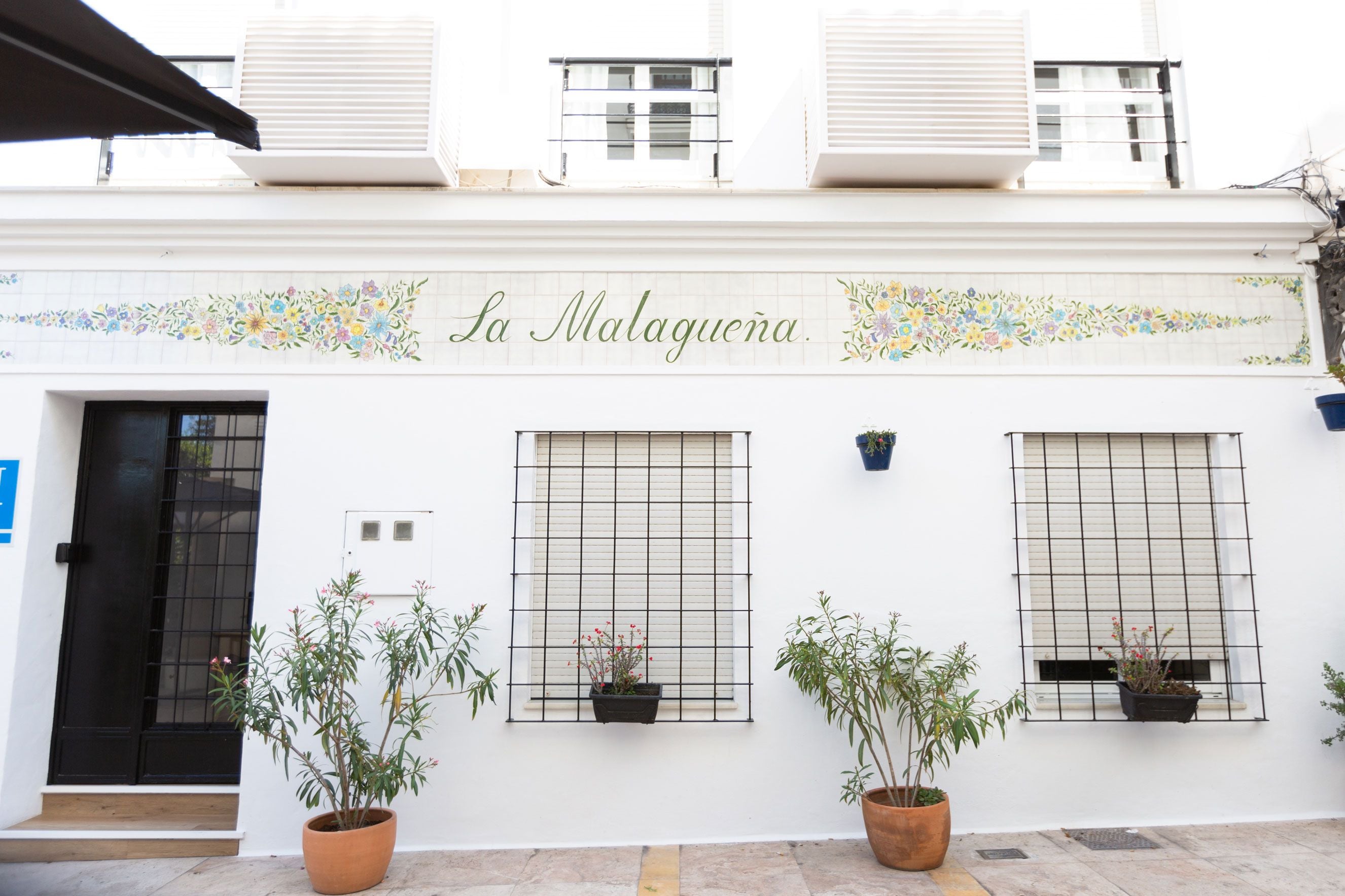 A building with a sign reading "La Malaguena" and three windows with potted plants.