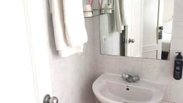 Un baño con lavamanos pedestal, espejo, toallero, cesto de basura y puerta.