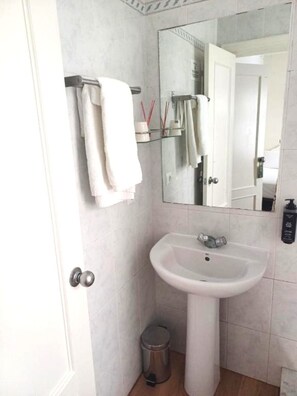 A bathroom with a pedestal sink, a mirror, a towel rack, a trash bin, and a door. - Hostal Boutique La Malagueña Only Adults by Croma (Estepona)