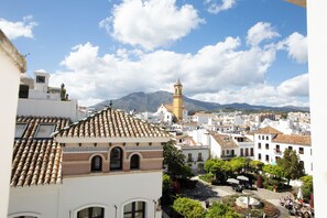 A town square with a fountain, surrounded by buildings with traditional architecture and a mountain in the background. - Hostal Boutique La Malagueña Only Adults by Croma (Estepona)